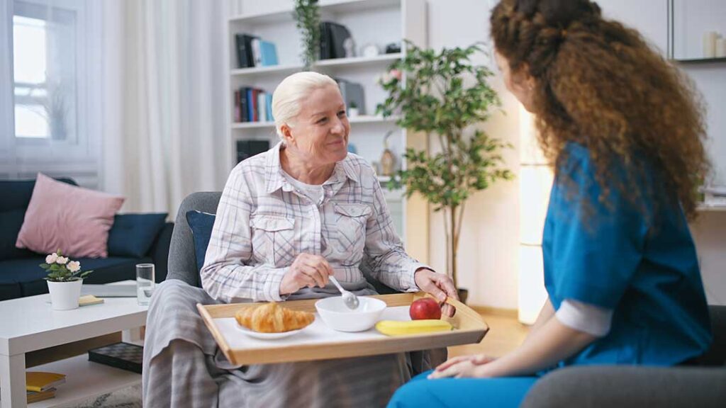 Older adult chatting with staff while seated in a comfortable, home-like assisted living common area.