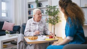 Older adult chatting with staff while seated in a comfortable, home-like assisted living common area.