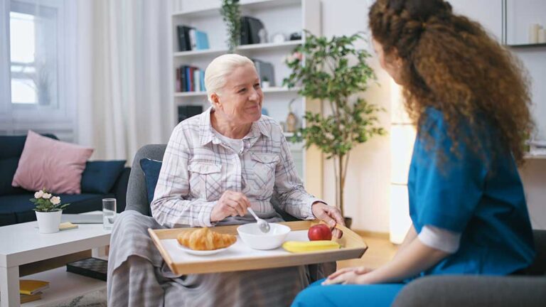 Older adult chatting with staff while seated in a comfortable, home-like assisted living common area.